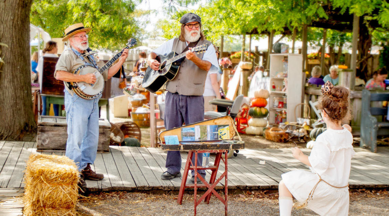 Two bluegrass musicians in denim perform for a young girl in a white dress