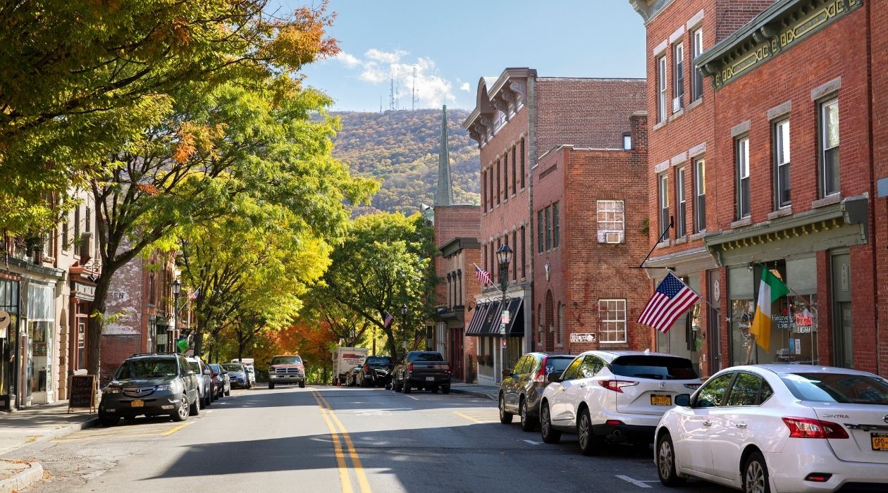 Main street with green trees on left side and brick buildings on right with blue mountains on horizon