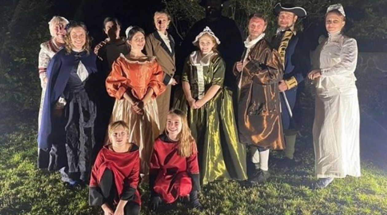 A group of 12 characters, 10 adults and 2 kids, wearing old fashioned clothing accurate for the characters they are portraying at the Legends By Candlelight event at Clermont State Historic Site in Germantown