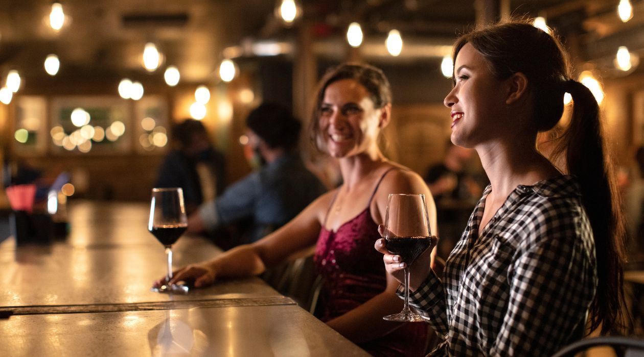 Two women sit at the bar smiling and enjoying glasses of red wine at 1915 Wine Cellar, Poughkeepsie